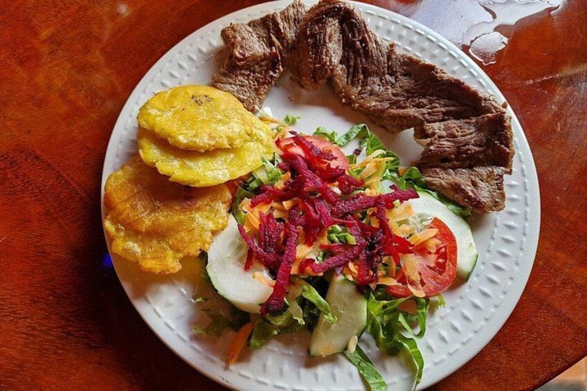 Un plato con carne de res, plátanos fritos y una ensalada. 3