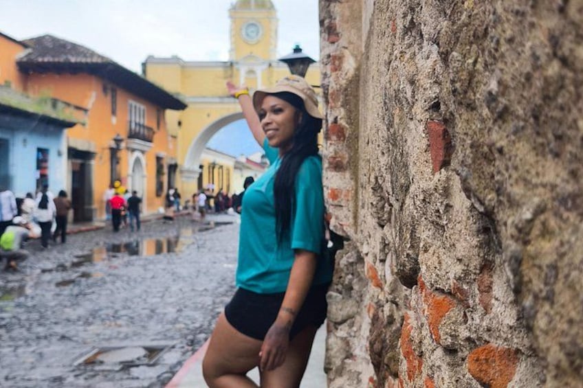 A person leaning against a brick wall in a cobblestone street with historic buildings and a clock tower in the background. 5