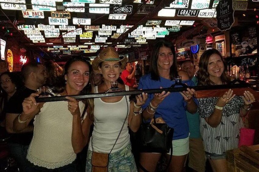 Un grupo de personas sosteniendo un objeto largo en un bar con letreros de neón al fondo. 3