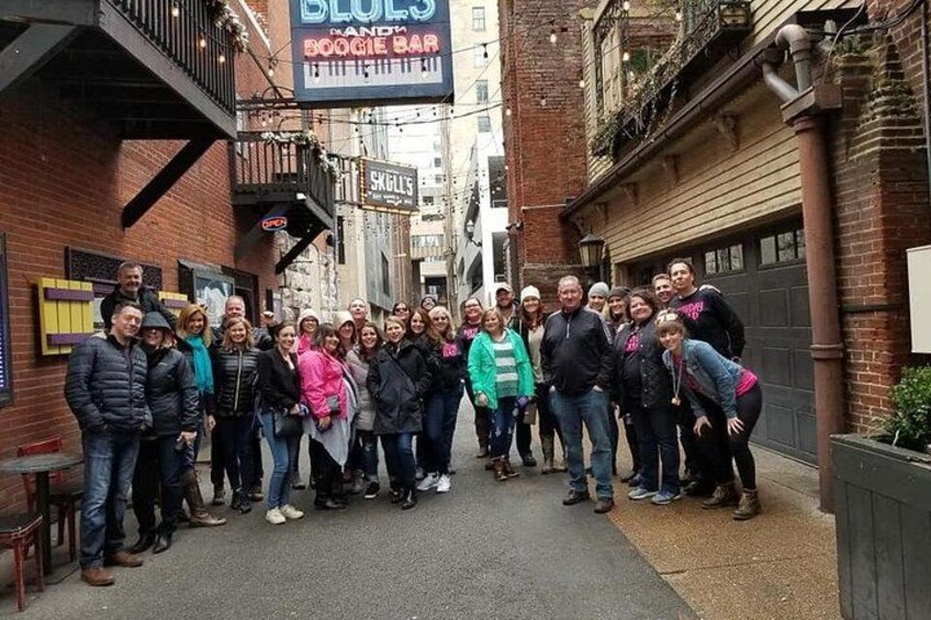 Un grupo de personas de pie en una calle, con un letrero que dice 'Blues and Boozy Bar' y otro que anuncia 'Skulls'. 4