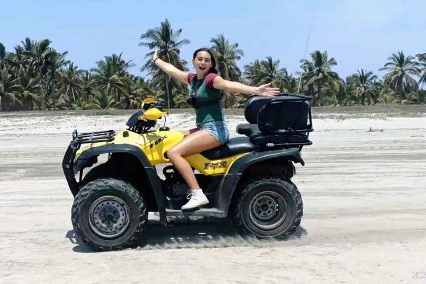 A person riding a yellow ATV on a sandy beach with palm trees in the background. 5