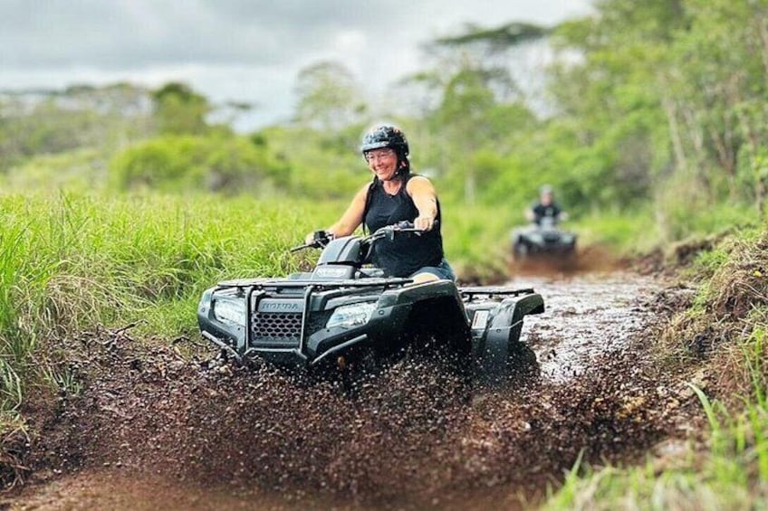 A person riding an ATV on a muddy path surrounded by greenery. 2