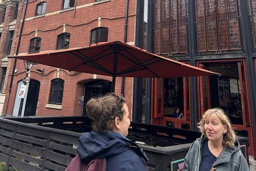 Two people standing in front of a brick building with a red awning. 4
