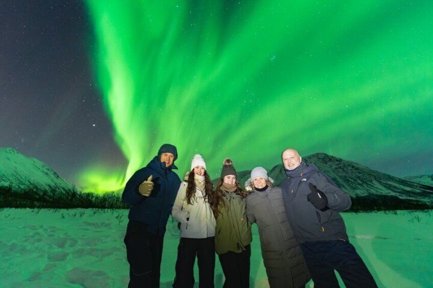 A group of people posing with the Northern Lights in a snowy landscape. 1