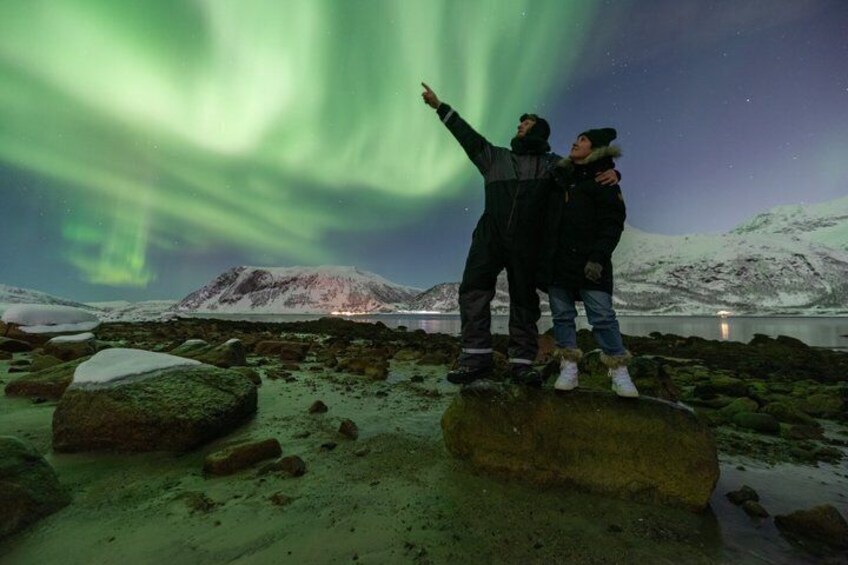 Two people standing on a rocky shore, gazing at the northern lights. 2