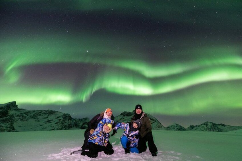 Two people posing with a backdrop of the Northern Lights over a snowy landscape. 4