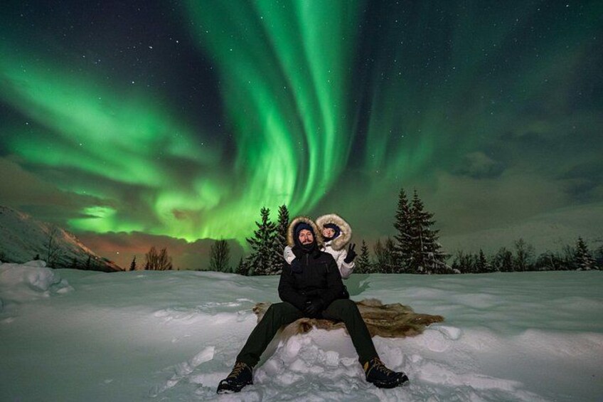 Two people sitting on snow with the aurora borealis in the background. 2