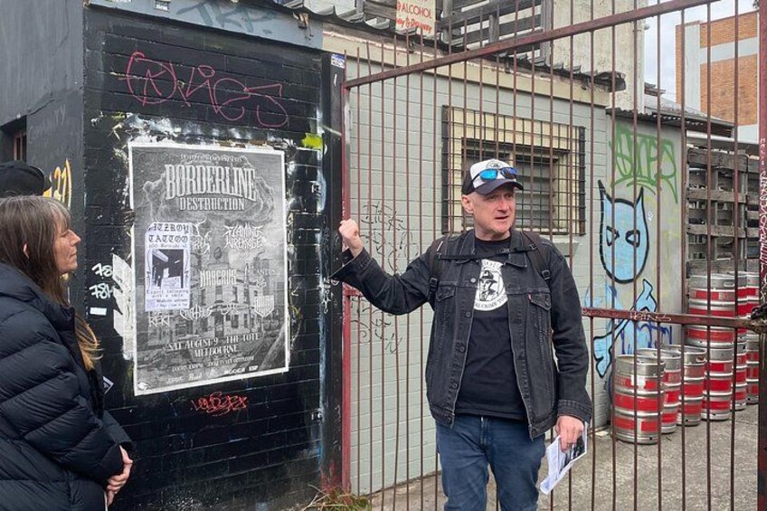 En mand peger på en plakat på en væg, graffiti og metalfade i baggrunden. 4