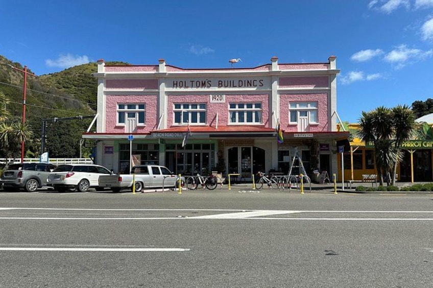 A pink and white building named 'Holtons Buildings' with a sign '1900' and a 'Beach Road Cafe' sign below. 3