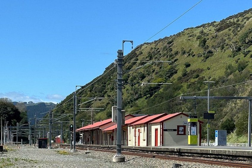 A railway station with tracks, a red-roofed building, and a mountainous backdrop. 2