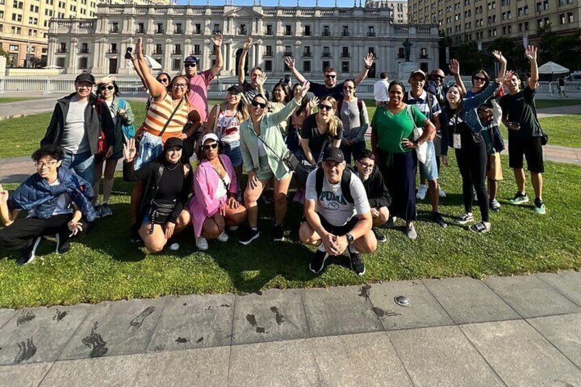 A group of people posing for a photo in a grassy area with a large building in the background. 2