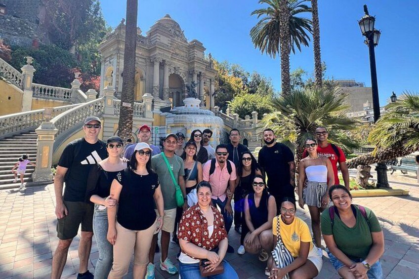 A group of people posing in front of a historic building with a fountain. 2