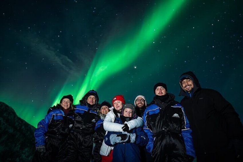 A group of people posing with a dog under a green aurora display. 1