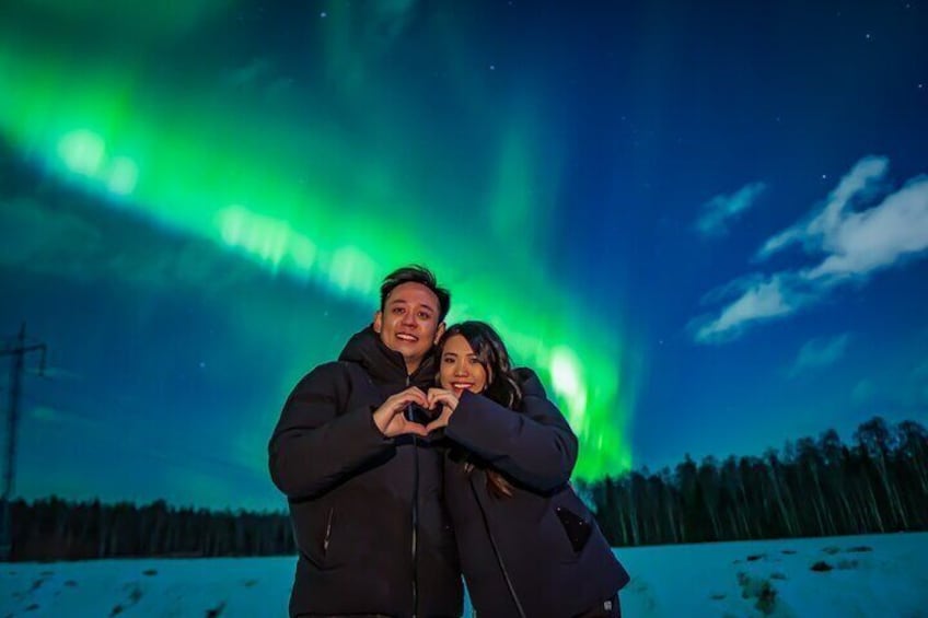 Two people making a heart shape with their hands under the Northern Lights. 3