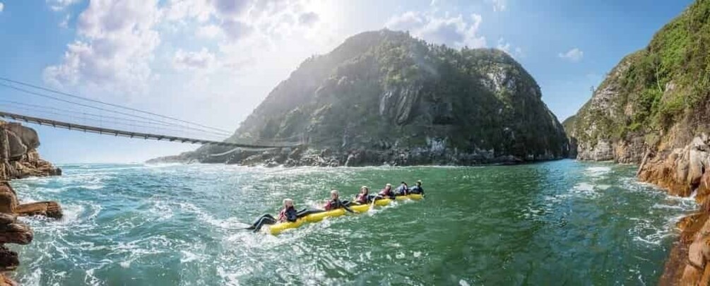 A group of people rafting on a river with a bridge in the background. 3