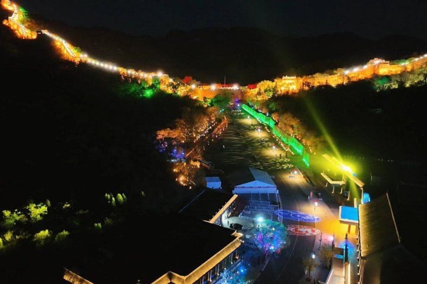 A brightly lit pathway with colorful lights, a building, and a hill in the background. 3
