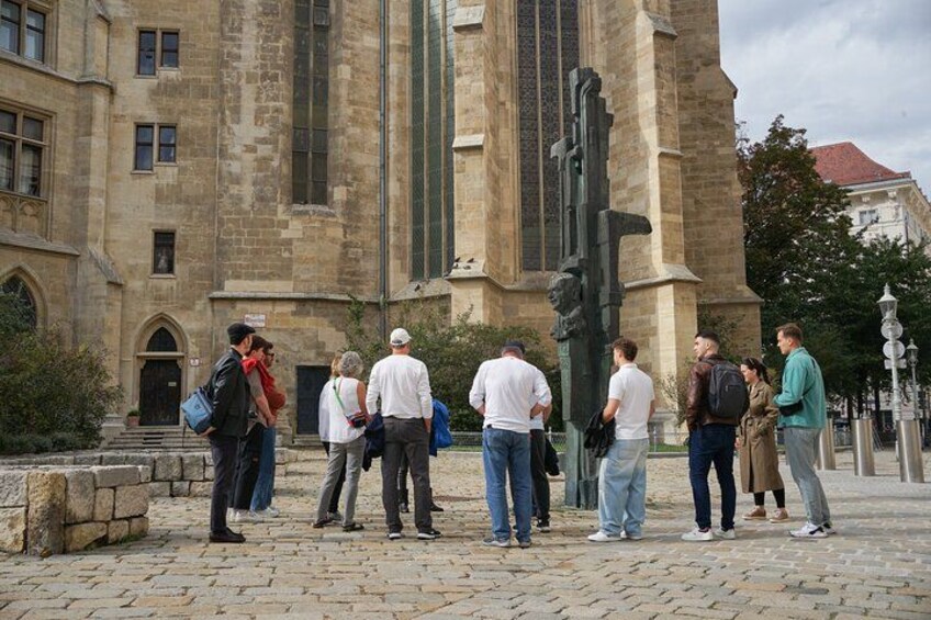 A group of people standing in front of a historic building with a large statue. 3