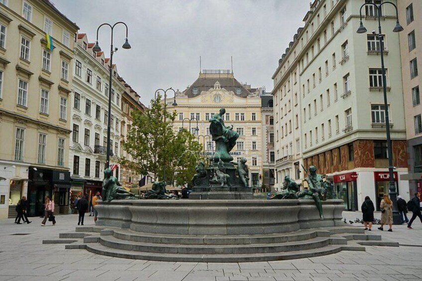 Une place publique avec une fontaine centrale, entourée de bâtiments historiques et fréquentée par des piétons. 2