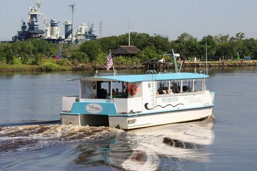 A boat with an American flag, moving on water with a military ship in the background. 4