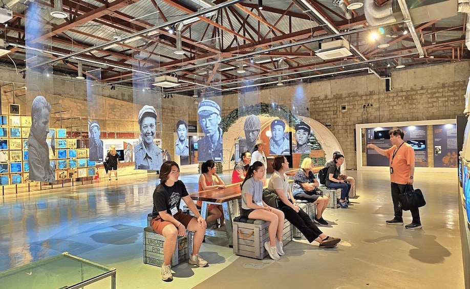 A museum interior with people sitting on benches, surrounded by large wall-mounted portraits and informational displays. 2