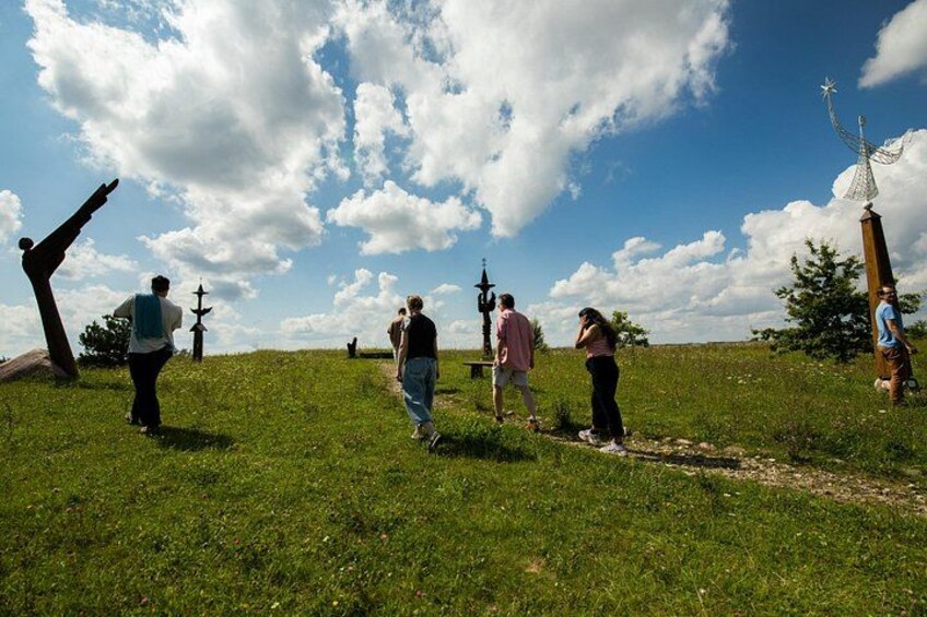 A grassy hill with people walking, a large sculpture, and a cross. 3