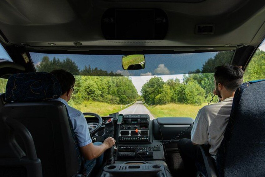 A vehicle interior with two people seated, a steering wheel, dashboard, and a road ahead. 5