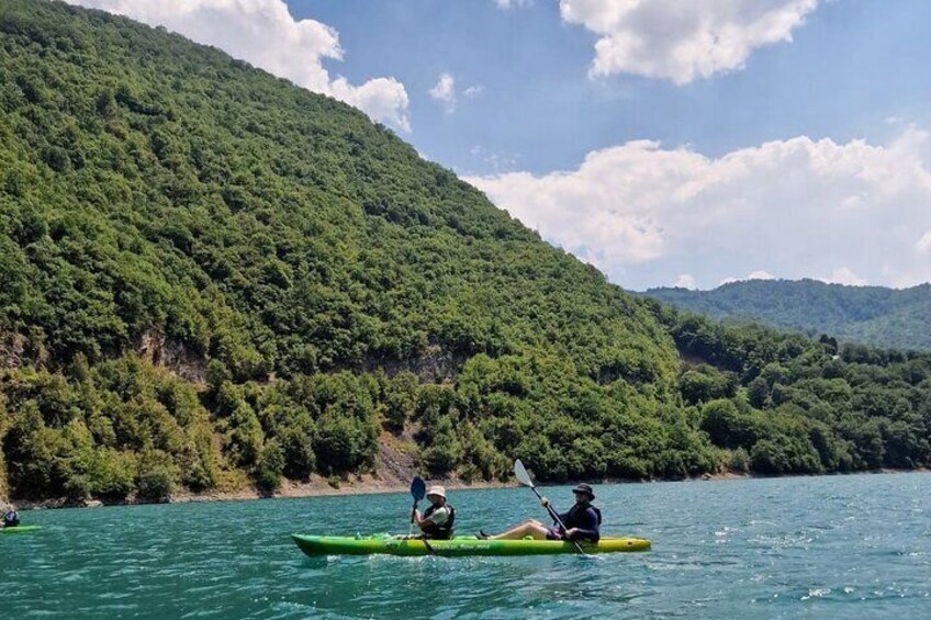 Two people kayaking on a calm lake surrounded by lush green hills. 3