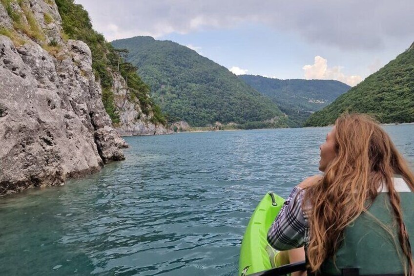 A person kayaking on a calm lake surrounded by rocky cliffs and lush green mountains. 5