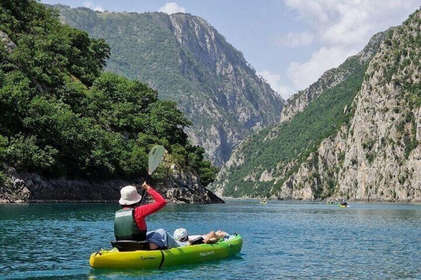 A person kayaking on a calm river surrounded by lush green mountains. 1