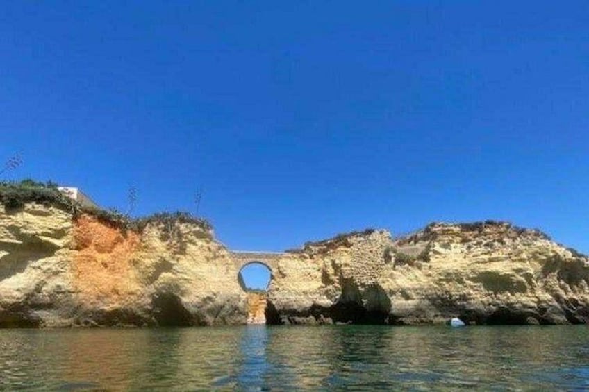 A coastal landscape with a circular stone structure, a clear blue sky, and calm water. 3