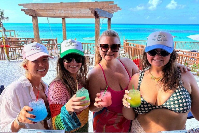 A beach with a wooden structure, clear blue water, and people holding drinks. 5