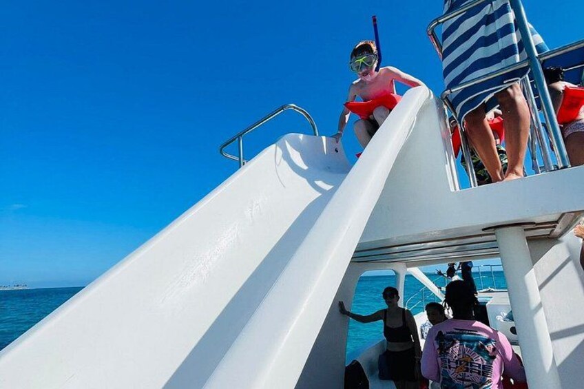A boat with a white slide, people on it, and the ocean in the background. 3
