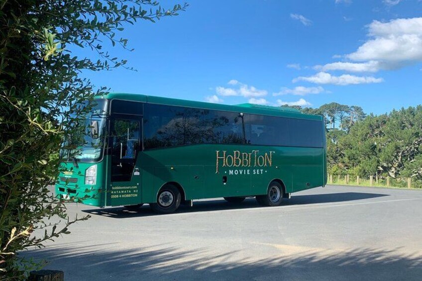 En grøn bus med teksten 'Hobbiton Movie Set' på siden holder parkeret på en vej. 5