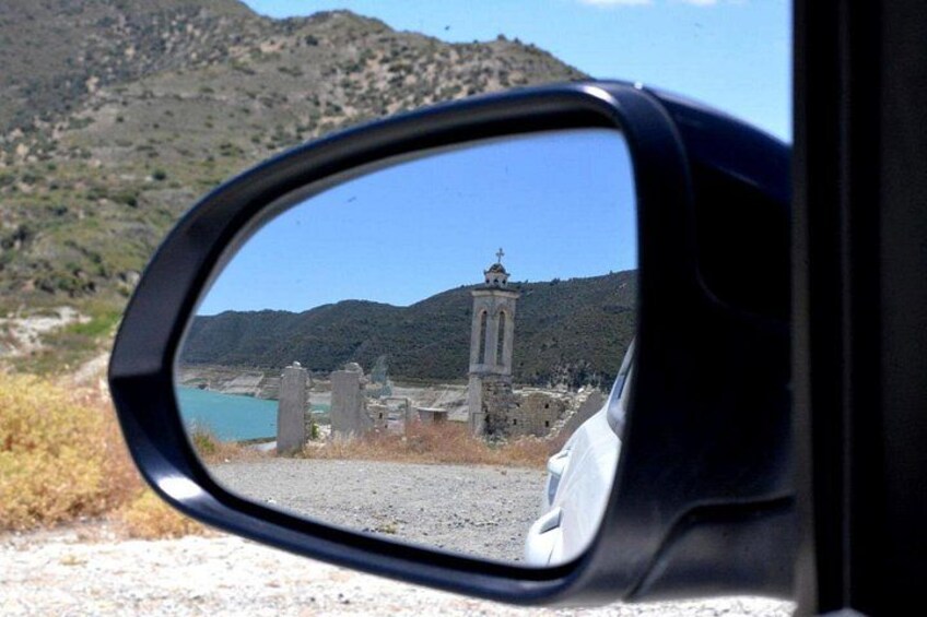 A car's side mirror reflecting a mountainous landscape with a church and a bridge. 4