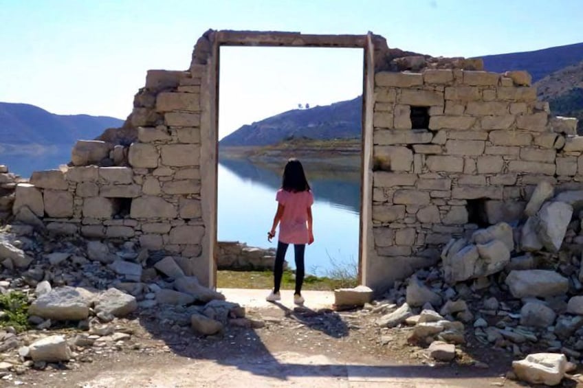 A person standing at the entrance of a stone structure with a lake in the background. 2