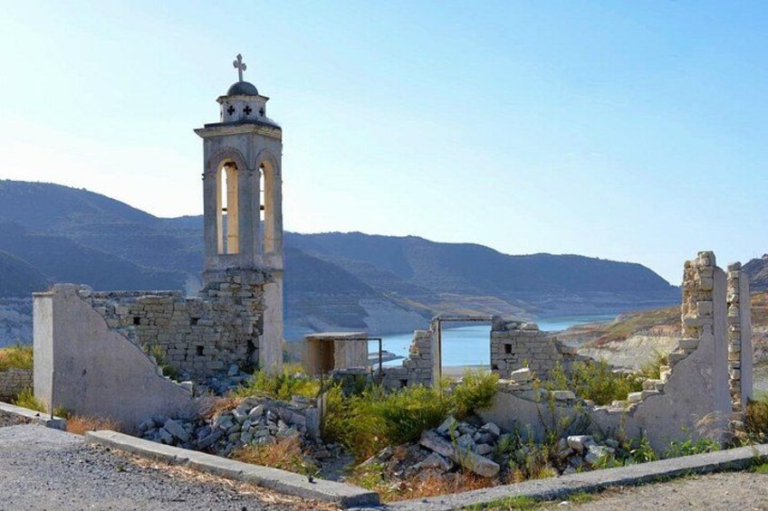 A coastal ruin with a bell tower, stone walls, and a clear view of the sea and mountains in the background. 3
