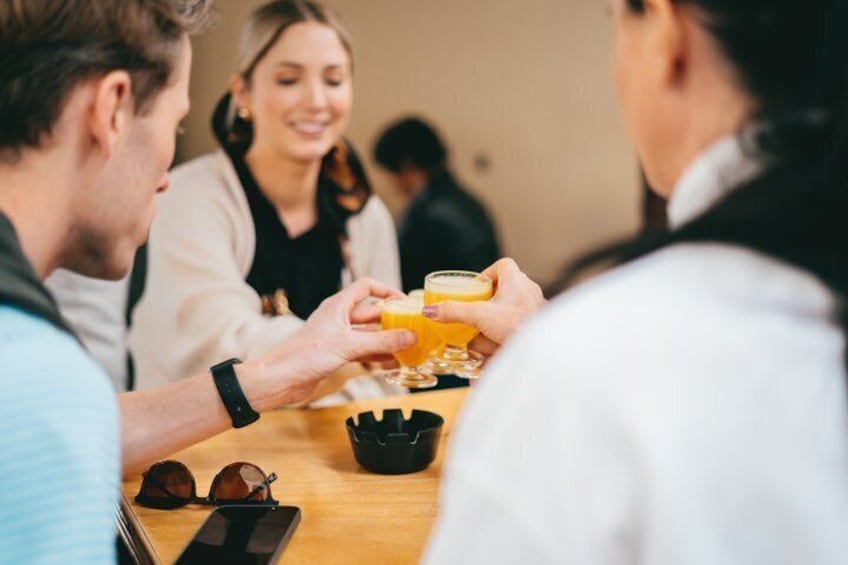 Een groep mensen zit rond een tafel, met glazen waarin een geel drankje staat, mogelijk jus d'orange. 2
