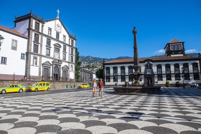 A plaza with patterned pavement, a fountain, and a historic building with a bell tower. 2