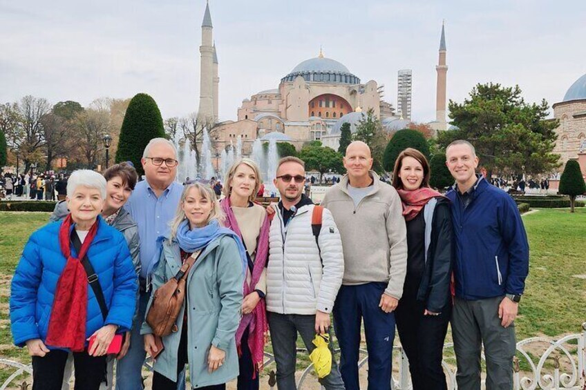 Un grupo de personas de pie en un parque, con un gran edificio y minaretes al fondo. 1