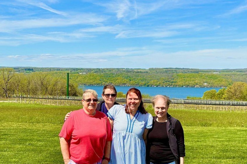 A group of people standing on a grassy field with a lake and hills in the background. 3
