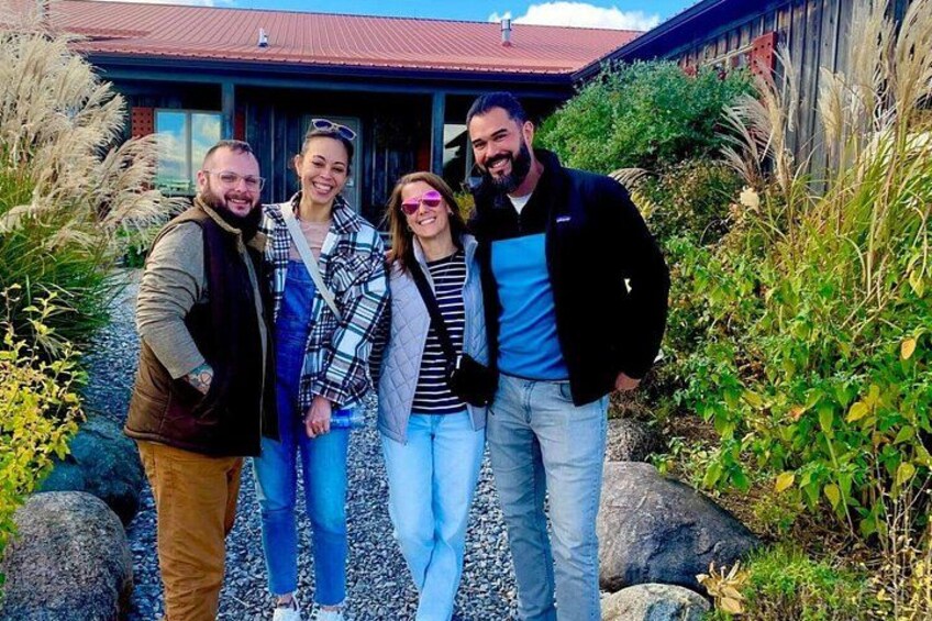Four people standing in front of a building with a red roof, surrounded by rocks and plants. 2