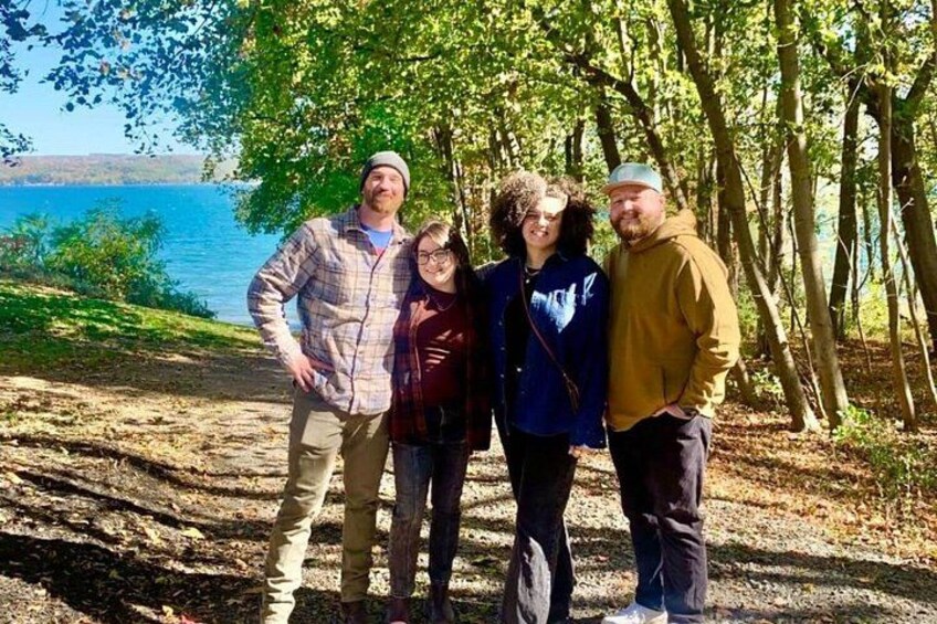 A group of people standing on a dirt path with trees and a body of water in the background. 4
