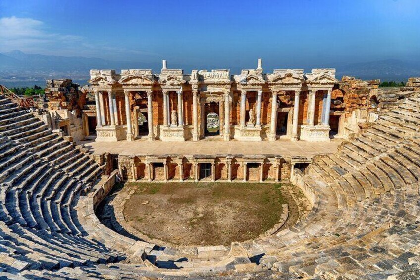 An ancient amphitheater with a central stage and tiered seating. 1