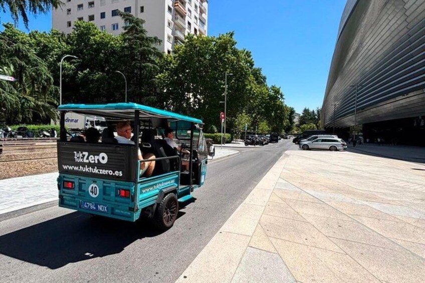 A turquoise tuk-tuk with passengers on a city street. 5