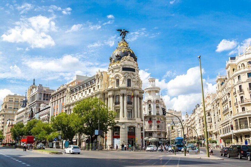 A historic building with ornate architecture, a street with cars and pedestrians, and a clear blue sky. 2