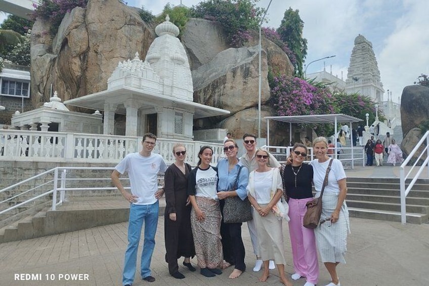 A group of people standing in front of a temple with a large rock and a white structure behind them. 4
