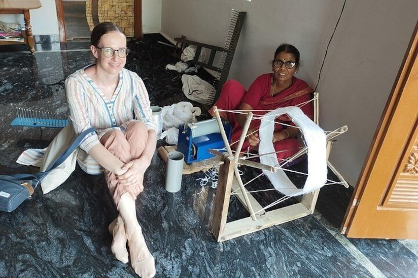 Two people sitting on the floor in a room with a marble floor, surrounded by various items including a wooden chair, a blue box, and a white cloth. 1