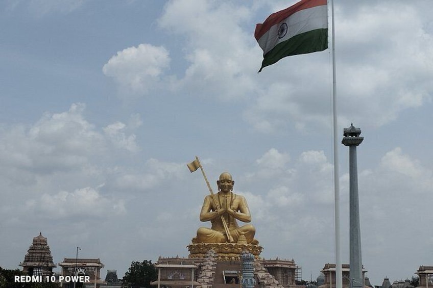 A golden statue of a seated figure with a flag, set against a cloudy sky with traditional architecture in the background. 5
