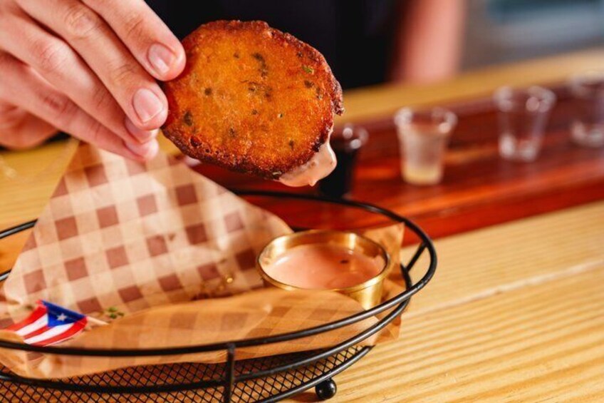 A person holding a round, golden-brown fried item, possibly a fritter, over a checkered cloth with a small American flag. 5