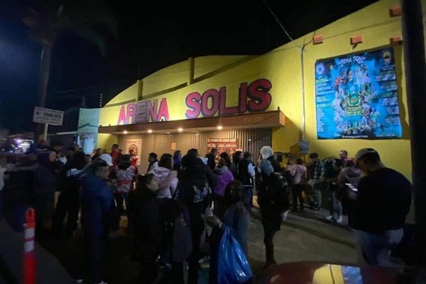 A crowded outdoor area with a building labeled 'ARENA SOLIS' and a large digital screen displaying an image. 2